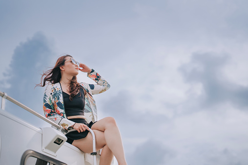Asian Chinese beautiful woman sitting on top of motor home campervan looking away with cool attitude