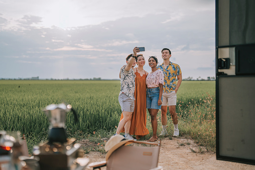 Asian Chinese gay couple and friends selfie in front of paddy field with phone camera