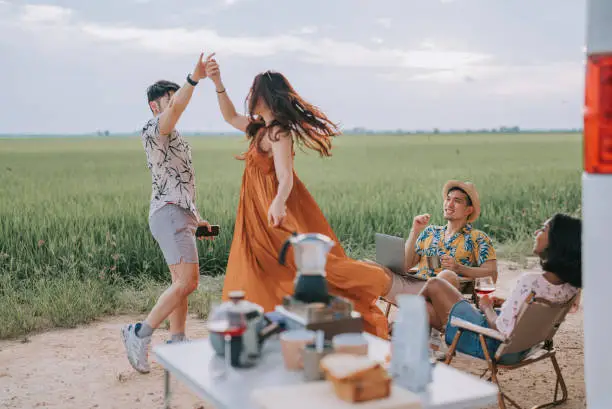 Photo of Asian chinese gay couple enjoying weekend leisure time with friends at rice paddy field travel with campervan dancing