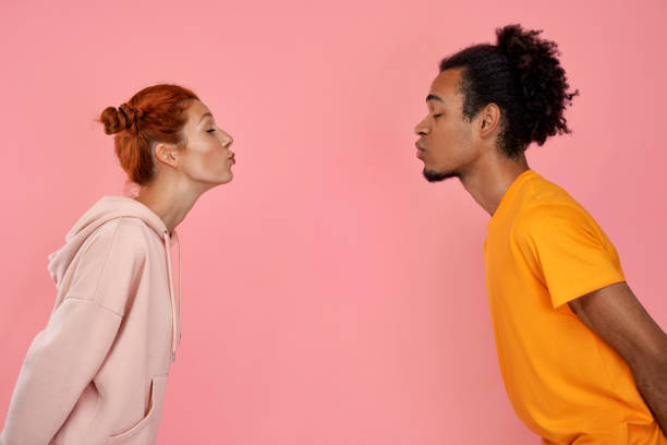 Profile of mixed race couple in love face each other, pout lips going to kiss, close eyes pleasure Profile photo of mixed race couple in love face each other, pout lips and going to kiss, close eyes from pleasure, dressed in stylish clothes, have date, over pink background. Romantic relationships. kissing stock pictures, royalty-free photos & images