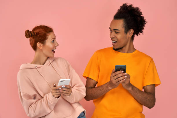 istock African American man and ginger woman smiling while both using mobile phones over pink background 1391723477