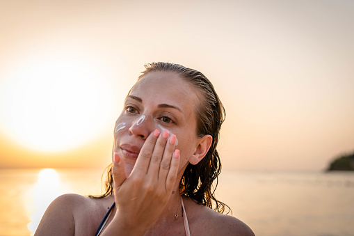 Young woman applying sunscreen while being outdoors, at the beach