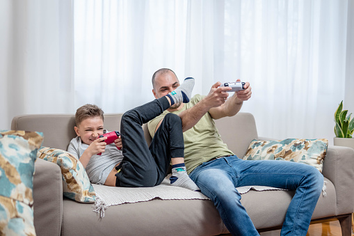 Joyful dad and son with joysticks playing video games at home