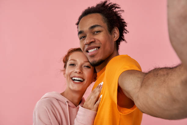 istock Mixed race couple ginger lady black guy couple make take selfie winking eyes pink studio background 1391723633
