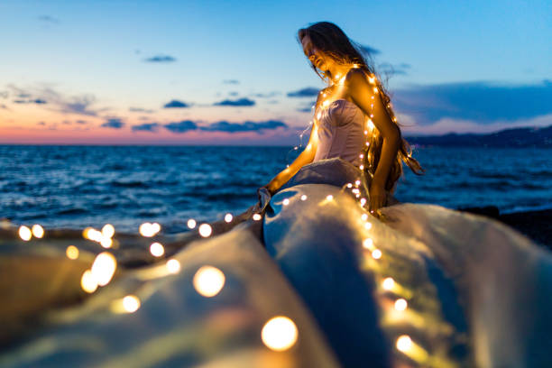 mulher de cabelos longos em espartilho com conchas no peito olhando lânguida no crepúsculo perto da praia do mar - mer people flash - fotografias e filmes do acervo