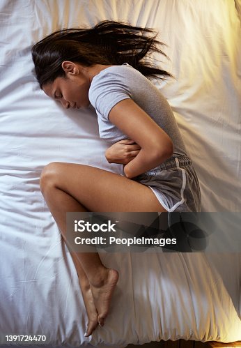 istock Full length shot of an attractive young woman lying alone on her bed and suffering from a tummy ache 1391724470