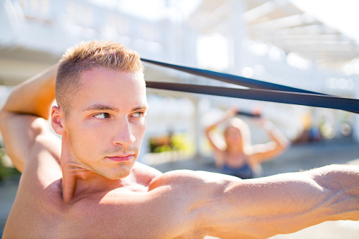 couple exercises with a resistance band outdoors in tropics .