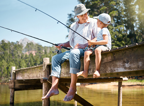 Photo of a little boy and his father spending quality time together while fishing on the riverbank