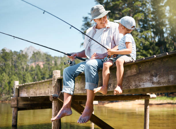 tiro de um menino pescando com seu avô em um lago em uma floresta - fishing lake grandfather grandson - fotografias e filmes do acervo