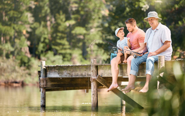 photo d’un petit garçon pêchant avec son père et son grand-père dans un lac dans une forêt - fishing lake grandfather grandson photos et images de collection