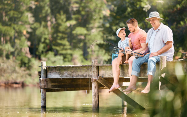 tiro de um menino pescando com seu pai e avô em um lago em uma floresta - fishing lake grandfather grandson - fotografias e filmes do acervo