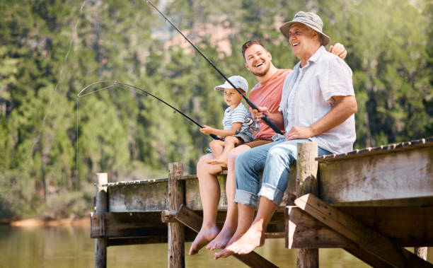 tiro de um menino pescando com seu pai e avô em um lago em uma floresta - fishing lake grandfather grandson - fotografias e filmes do acervo