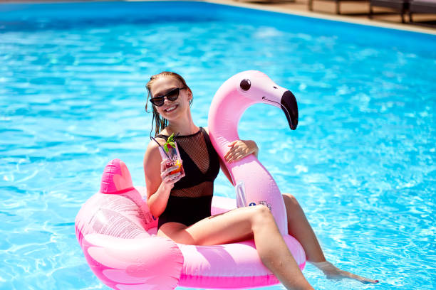 Hot slim woman in bikini chilling with cocktail on inflatable pink flamingo float at swimming pool. Fit girl in swimwear lies in the sun and drinks on floaty. Pretty female on tropical vacation Hot slim woman in bikini chilling with cocktail on inflatable pink flamingo float at swimming pool. Fit girl in swimwear lies in the sun and drinks on floaty. Pretty female on a tropical vacation. swimwear bikini top bikini bikini bottom stock pictures, royalty-free photos & images