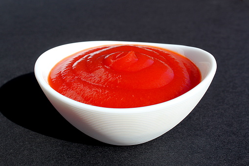 Tomato sauce is poured into a white plate on a black background