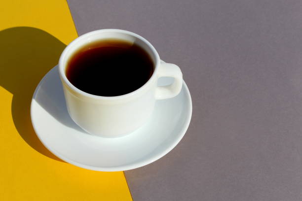 A fresh coffee drink in a white cup stands on a yellow and gray background at the same time.