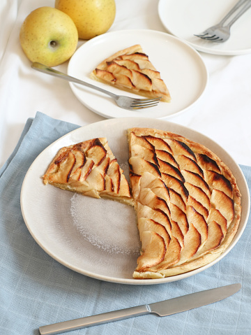 Pieces of a classic traditional French apple tart fine(tarte fine aux pommes) caramelized with brown sugar in a plate. With its fruit and fork in background. This tart made with butter puff pastry