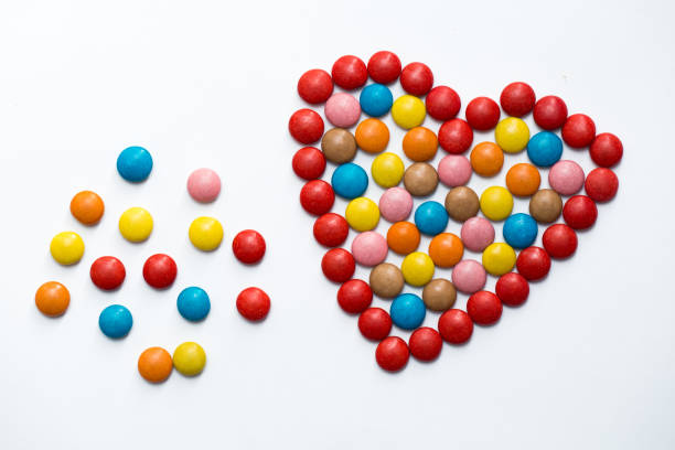 colorful m&m button chocolate candies in the love shape on white background. - candy coated imagens e fotografias de stock