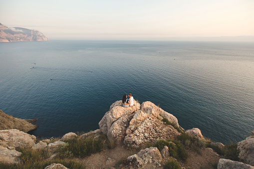 Lovers, guy and girl, on the edge of the cliff against the backdrop of mountains and ocean.