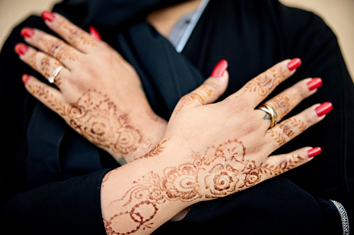Portrait of Middle Eastern woman in black abaya displaying intricate designs on manicured hands created for special occasion or celebration event.