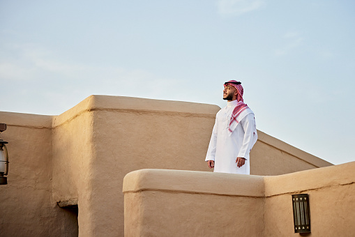 Waist-up view of bearded Middle Eastern man in traditional attire at UNESCO World Heritage Site near Riyadh and looking away from camera. Property release attached.