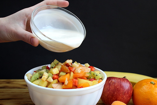 Fruit salad in a plate, a woman's hand starts pouring yogurt