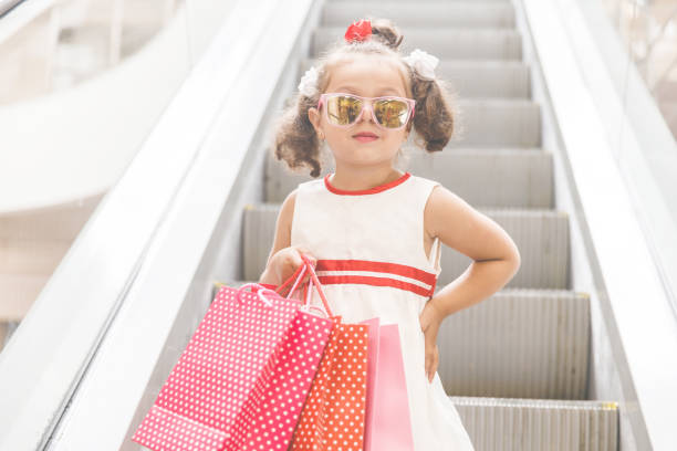 menina de óculos escuros na escada rolante no shopping com compras - escalator child shopping mall little girls - fotografias e filmes do acervo