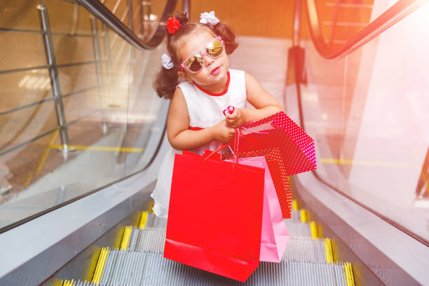 色とりどりのバッグを持つモールのエスカレーターでサングラスをかけた小さな女の子 - escalator child shopping mall little girls ストックフォトと画像