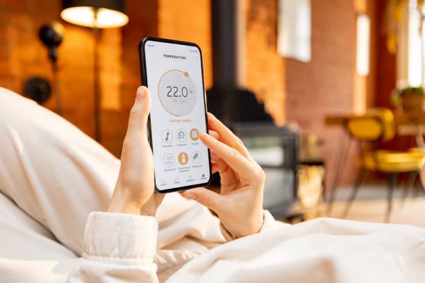 frau hält telefon mit laufender smart-home-anwendung zur temperaturregelung - remote area stock-fotos und bilder