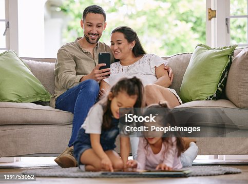 istock Shot of a young couple using a phone while their daughters read a book at home 1391753052