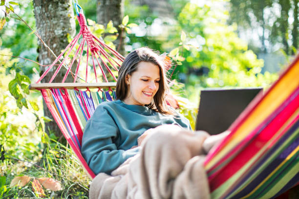 istock Young woman working with laptop from backyard in hammock 1391754541