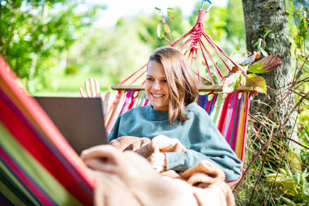 istock Young woman working with laptop from backyard in hammock 1391754558