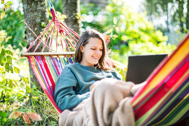 istock Young woman working with laptop from backyard in hammock 1391754590