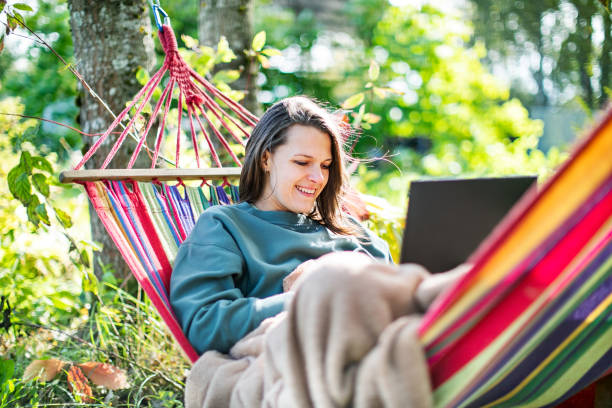 Young woman working with laptop from backyard in hammock Young woman working with laptop from backyard in hammock hammock relaxation women front or back yard stock pictures, royalty-free photos & images