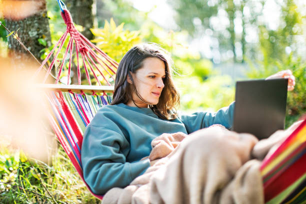 istock Young woman working with laptop from backyard in hammock 1391755173