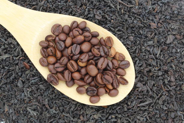 istock Coffee beans on a spoon lie on loose black tea. 1391755191