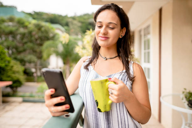istock Young woman drinking coffee and checking her phone on her patio 1391756088