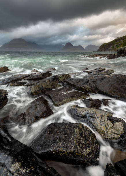 Moody Storm Clouds At Elgol, Isle of Skye, UK. Dramatic Cuillin seascape with dark storm clouds and crashing waves on rocks in foreground. Elgol, Isle of Skye, Scotland, UK. elgol beach stock pictures, royalty-free photos & images