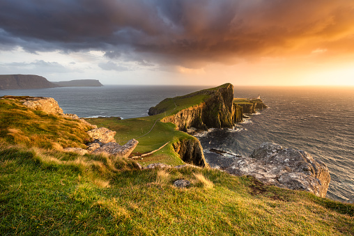 Beautiful evening light with dark dramatic storm clouds in sky at Neist Point lighthouse on The Isle of Skye, Scotland, UK. A group of rocks can be seen in the foreground which leads the eye into this iconic Hebridean landscape/seascape.
