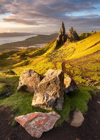 Breathtaking view of popular Scottish travel destination; The Old Man of Storr on the Isle of Skye. Dramatic clouds cover the morning sky with vibrant colours from the sunrise in the foreground.