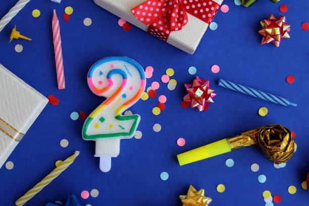 Candle with number 2 with holiday paraphernalia lie on a blue background.