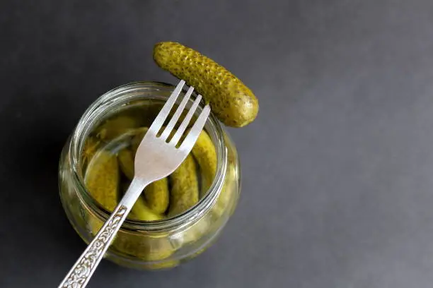 On a black background is a jar of pickled cucumbers and a fork.