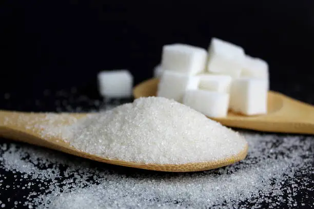 Photo of Two wooden spoons of sugar lie on a black background.