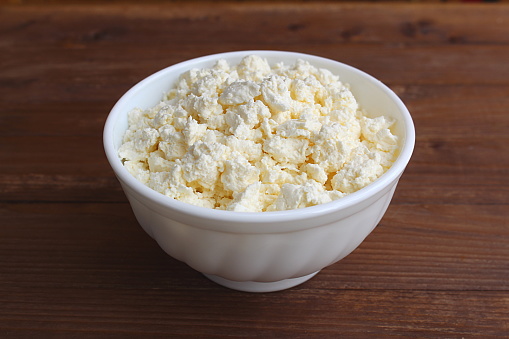 Fresh cottage cheese lies in a plate on a wooden table.