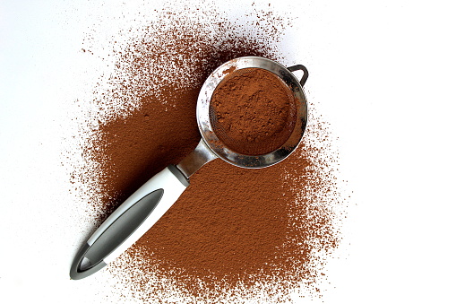 Scattered cocoa with a sieve lies on a white background.