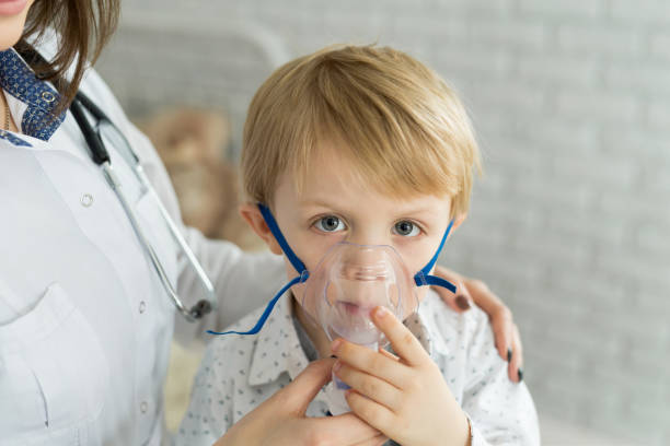 Medical doctor applying medicine inhalation treatment on a little boy with asthma inhalation therapy by the mask of inhaler Medical doctor applying medicine inhalation treatment on a little boy with asthma inhalation therapy by the mask of inhaler. pediatric nebulizer mask stock pictures, royalty-free photos & images