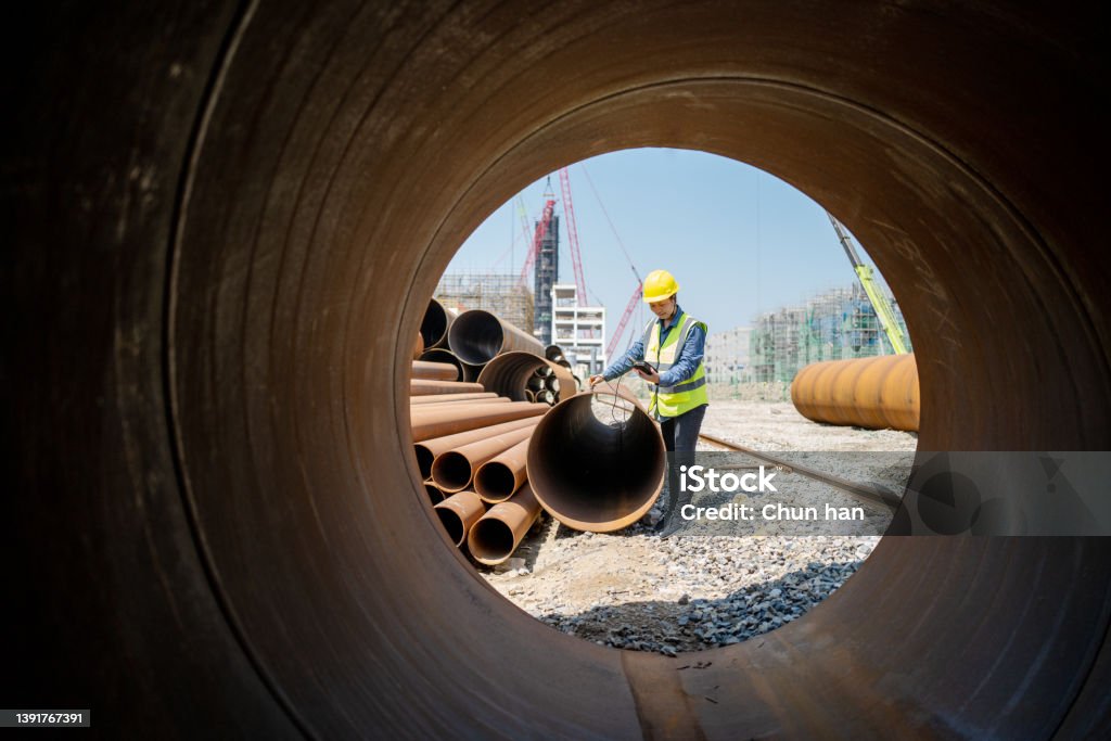 A female engineer used a measuring instrument to measure the quality of steel pipe Construction Site Stock Photo