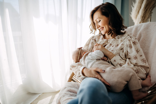 Mother breastfeeding a newborn baby, seating on rocking chair at  room.