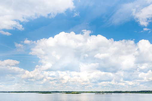 Cumulus clouds in the blue sky over the river in summer day