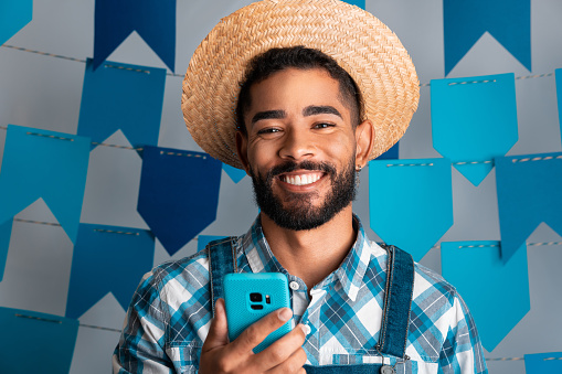 Festa Junina: party in Brazil, portrait of man with mobile phone at June Festival in caipira clothes