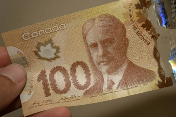 istock Persons hand giving the Currency of the Canada - One brown hundred dollar notes spread out on a brown background. Money exchange. 1391771237